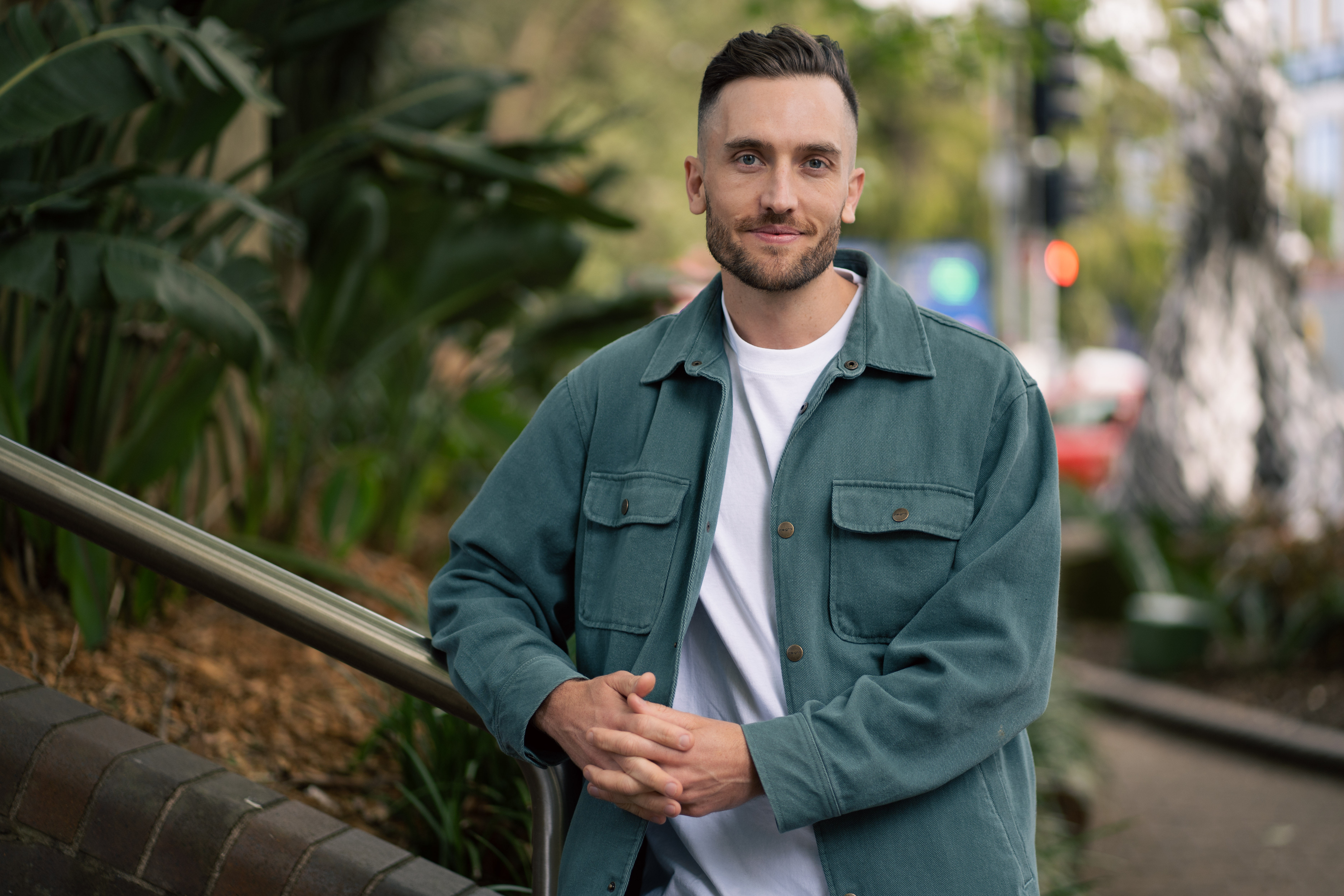 Andy Crebar leaning on a metal railing with a lush green garden background