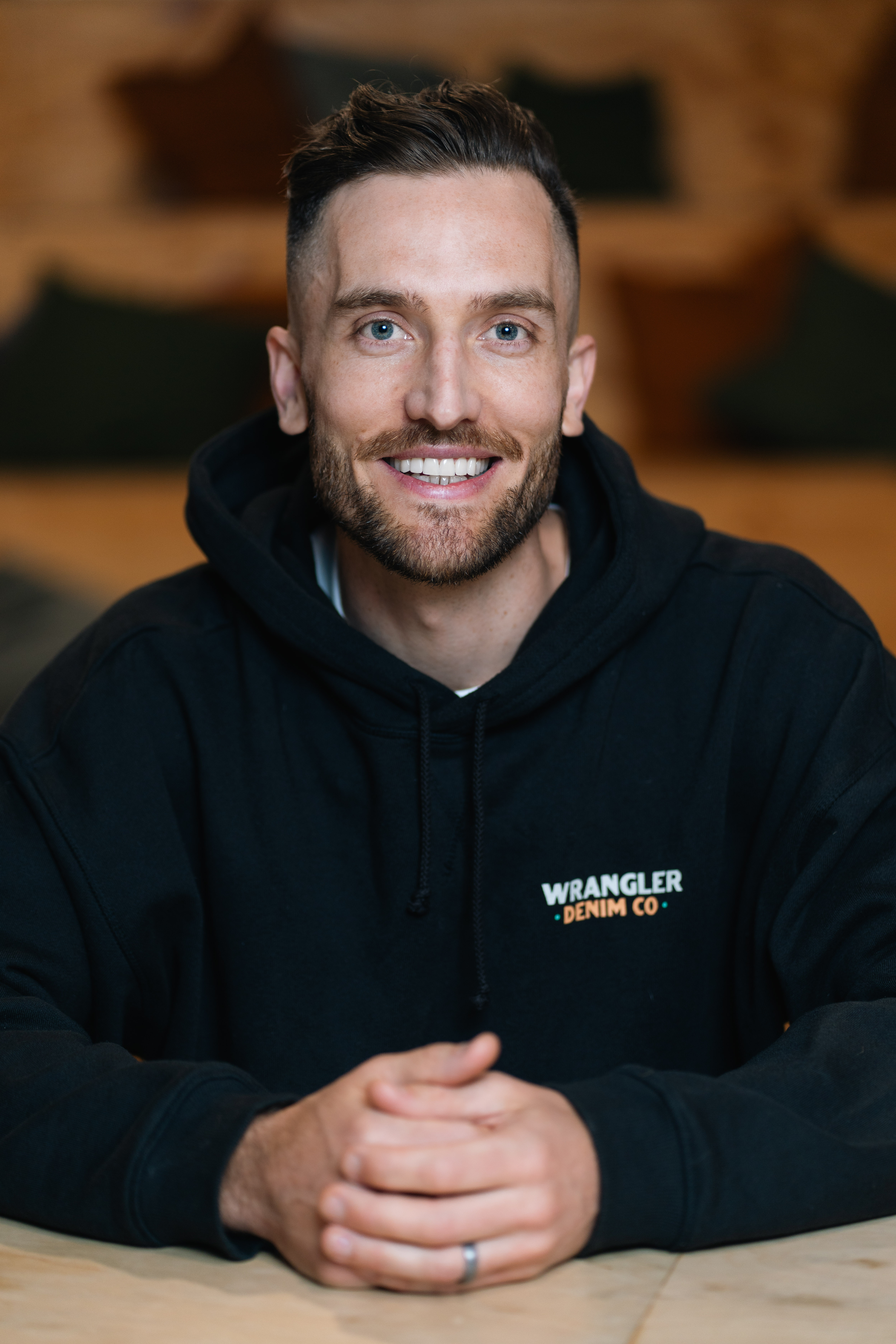 Close-up of Andy Crebar wearing a black hoodie sitting at a wooden table