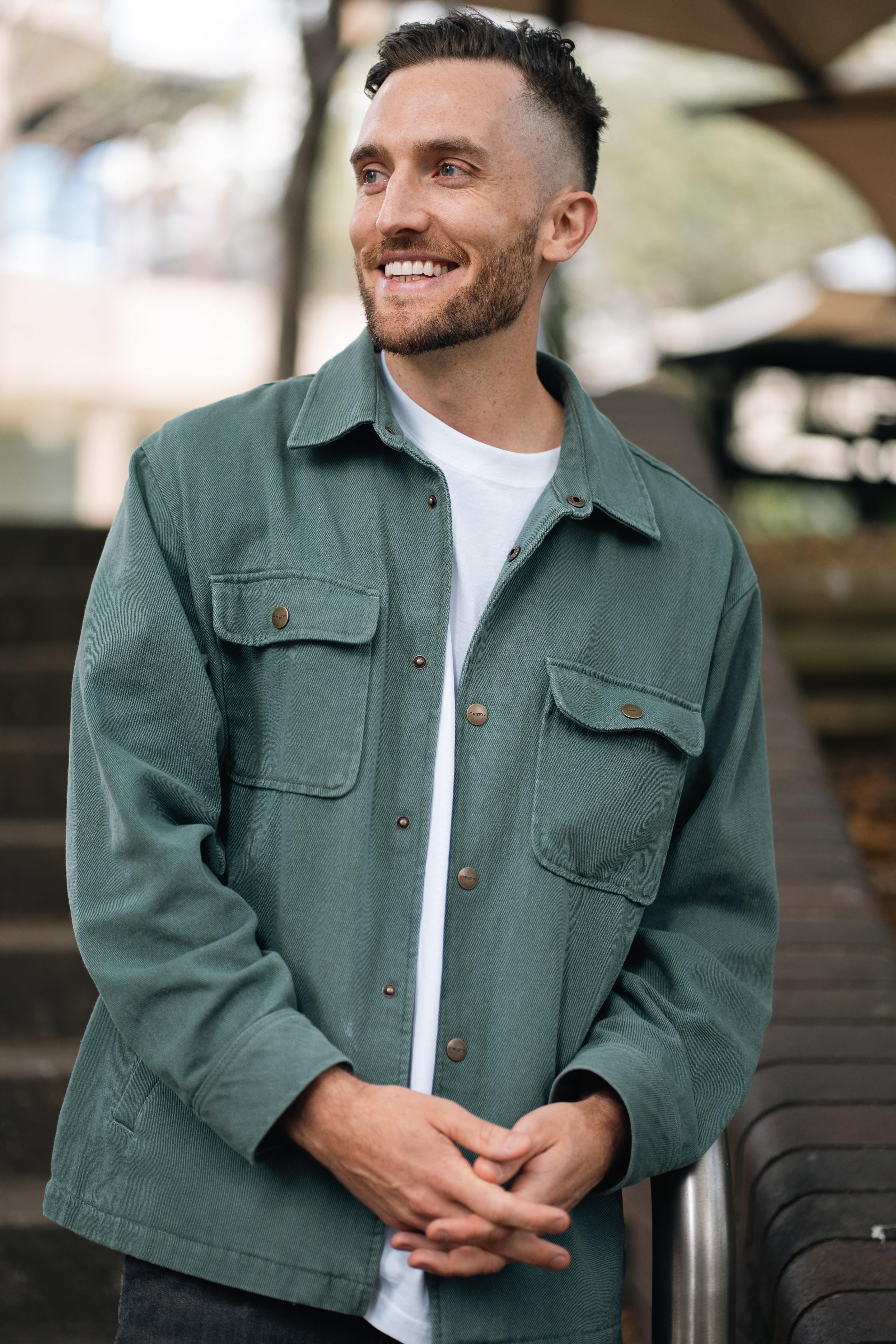 Casual outdoor portrait of Andy Crebar standing near stairs, wearing a green jacket and white t-shirt