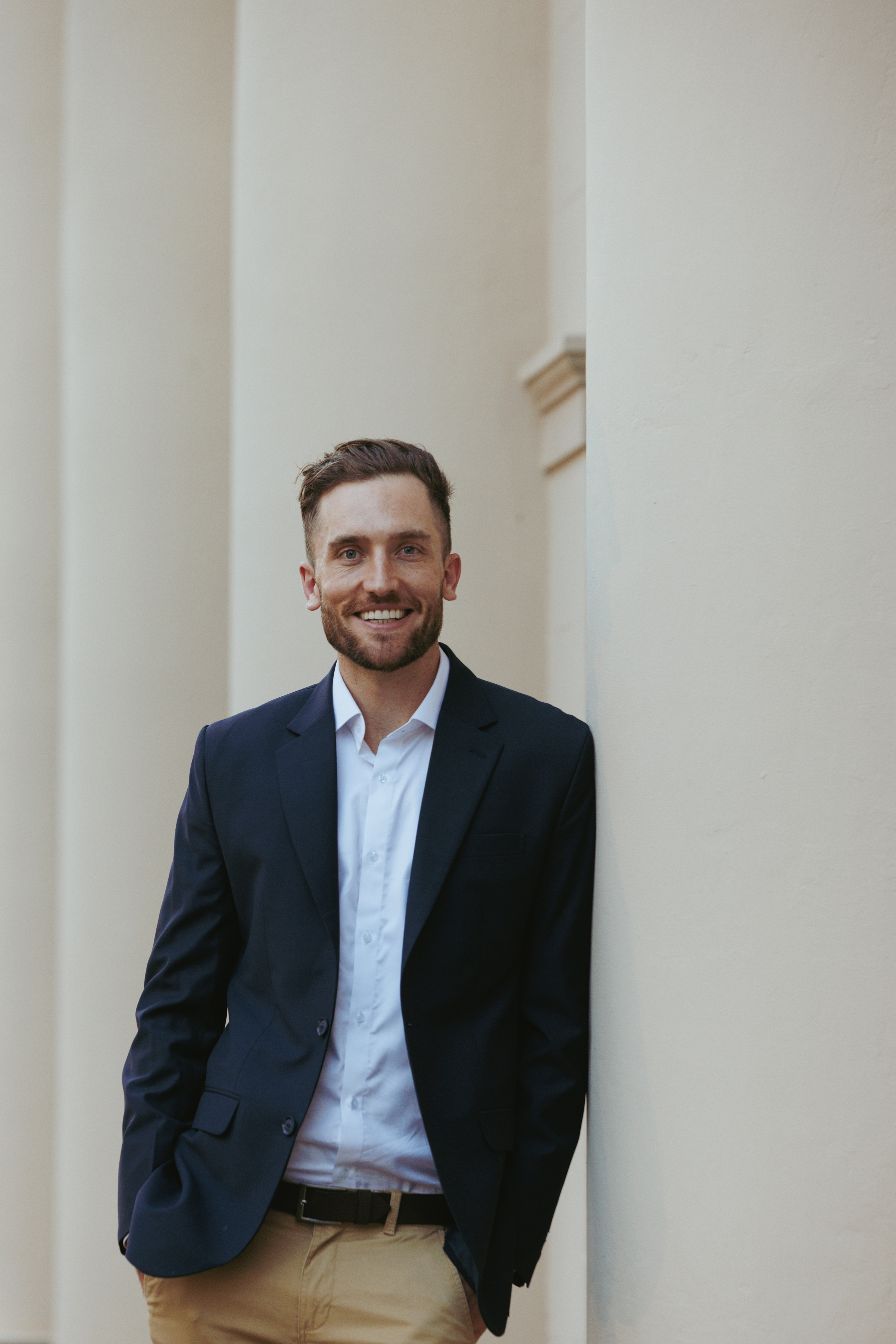 Andy Crebar leaning casually against a cream-coloured pillar in a navy suit