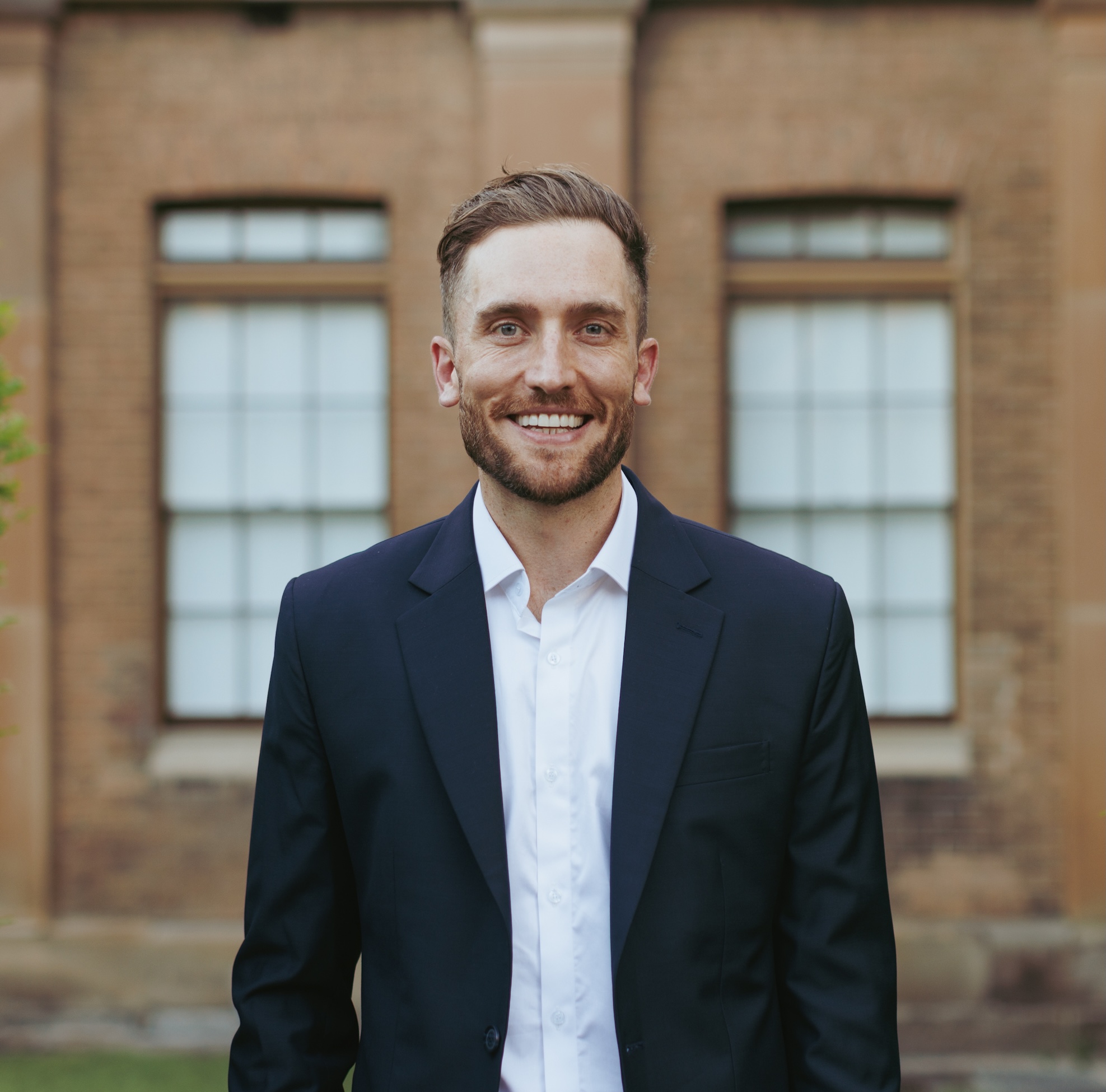 Andy Crebar smiling in a navy business suit standing in front of a heritage brick building